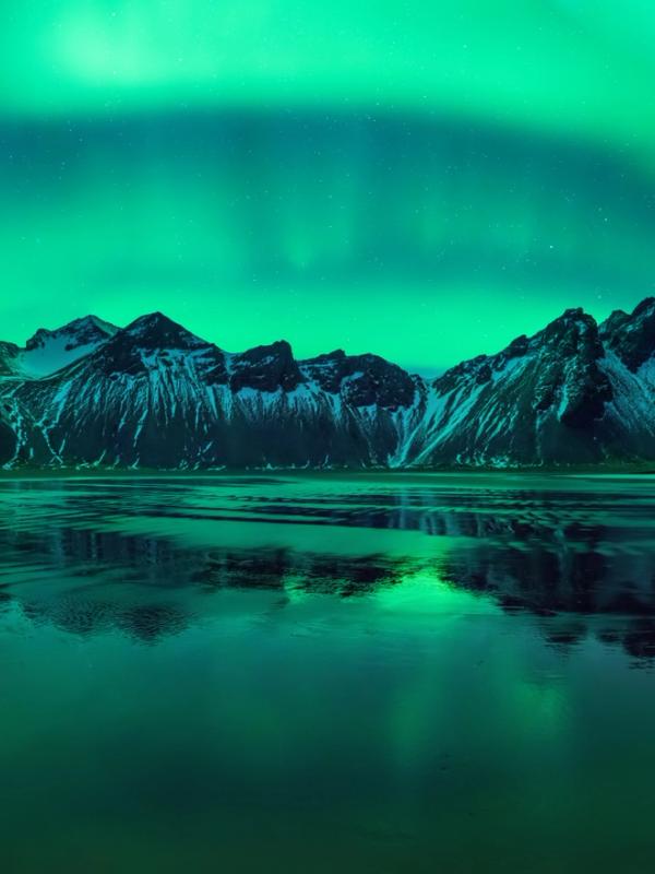 Reflejo en el agua de la aurora boreal encima de unas montañas.