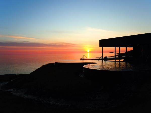 Atardecer naranja y azul sobre el océano, con un edificio en silueta y piscinas infinitas.