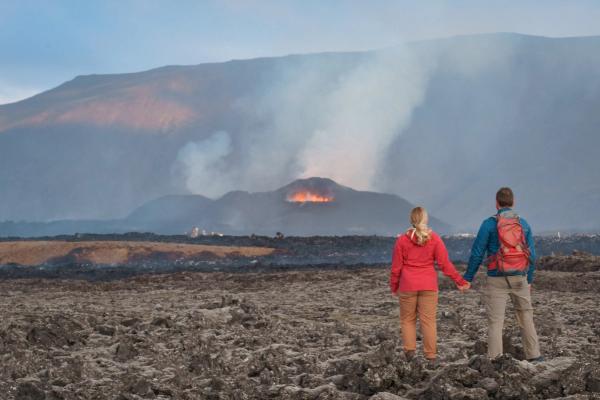 a man and a woman are holding hands while looking at a volcano .