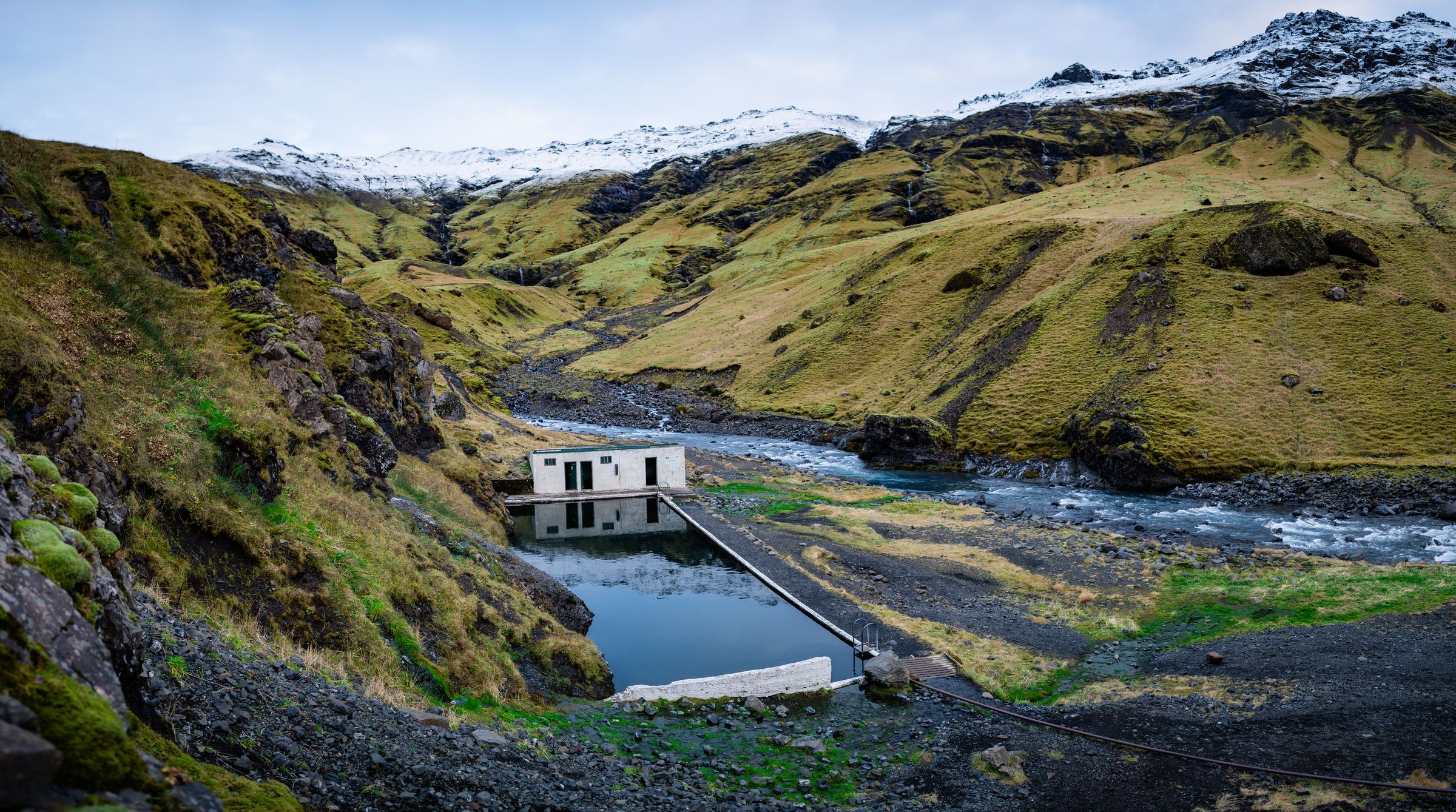 there is a small house in the middle of a valley next to a river at Seljavallalaug in iceland.