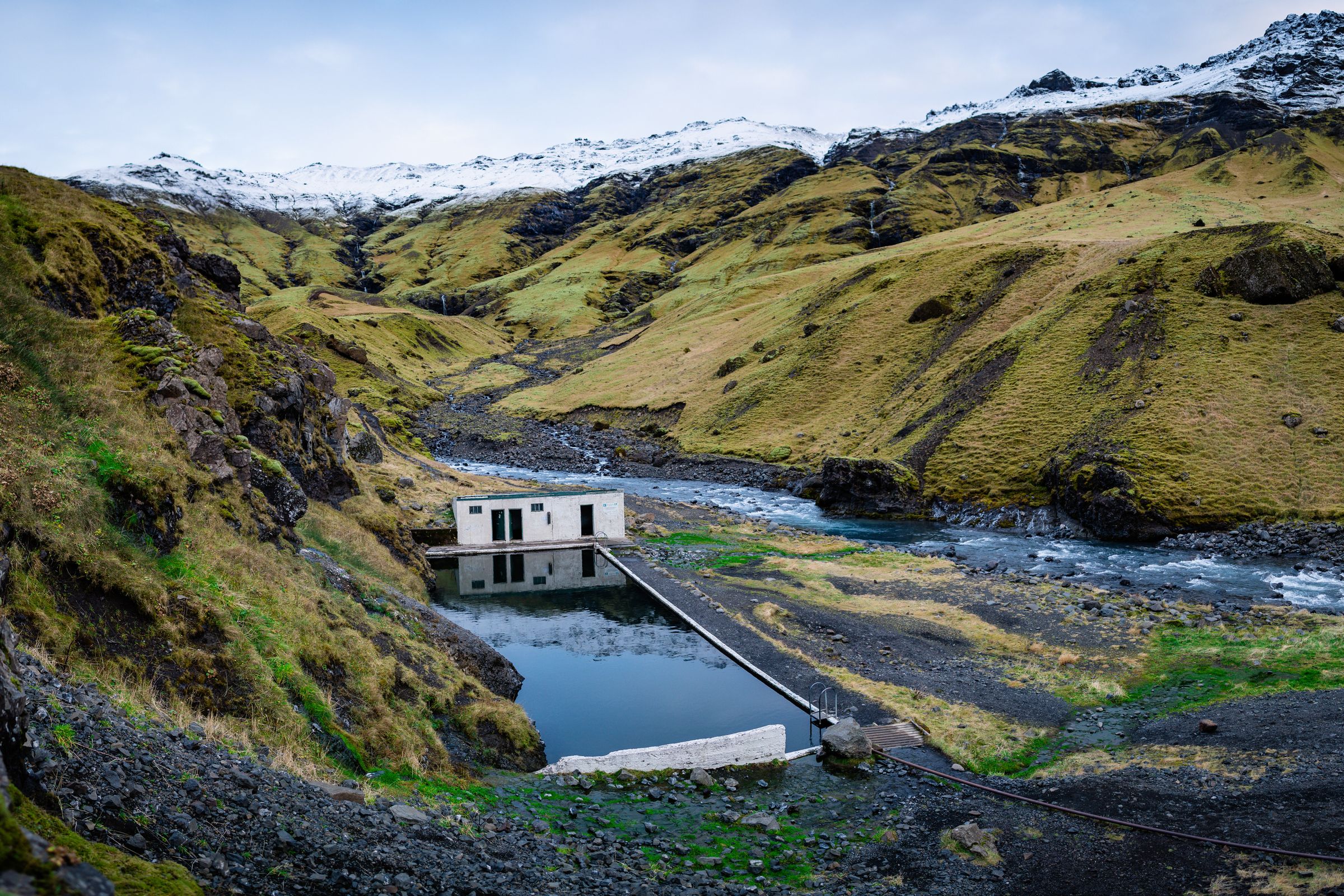 there is a small house in the middle of a valley next to a river at Seljavallalaug in iceland.