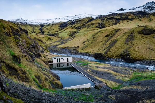 Il y a une petite maison au milieu d'une vallée à côté d'une rivière à Seljavallalaug en Islande.