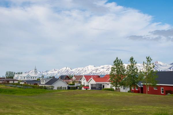 Un pueblo con casas coloridas y una iglesia blanca, un campo verde en primer plano y montañas nevadas en el fondo.
