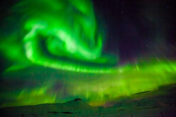 the aurora borealis is dancing in the night sky over a snowy mountain in iceland.