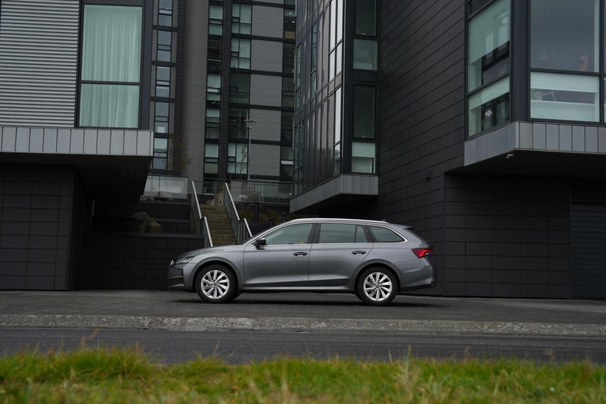 A silver station wagon parked in front of modern dark gray buildings.