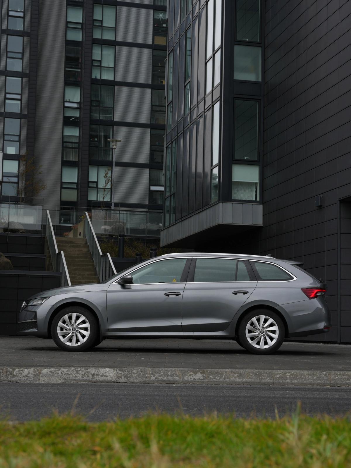 A silver station wagon parked in front of modern dark gray buildings.
