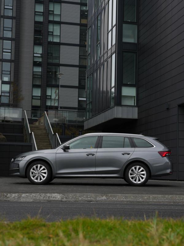A silver station wagon parked in front of modern dark gray buildings.