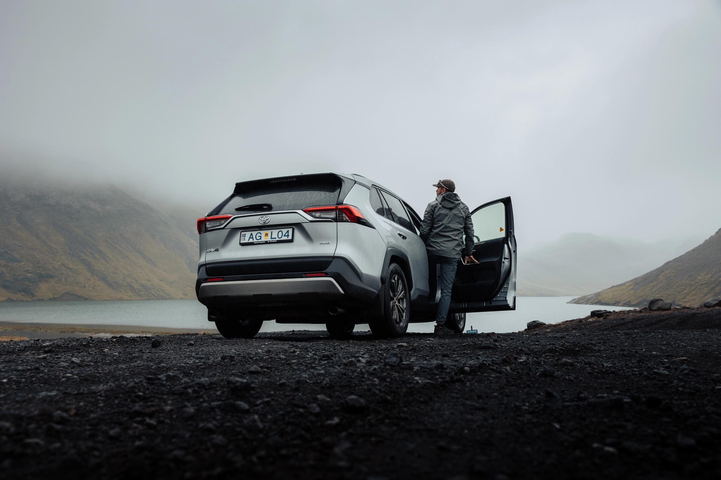 RAV4 avec vue sur le lac Vue arrière d’un Toyota RAV4 garé sur du gravier au bord d’un lac, avec la portière conducteur ouverte