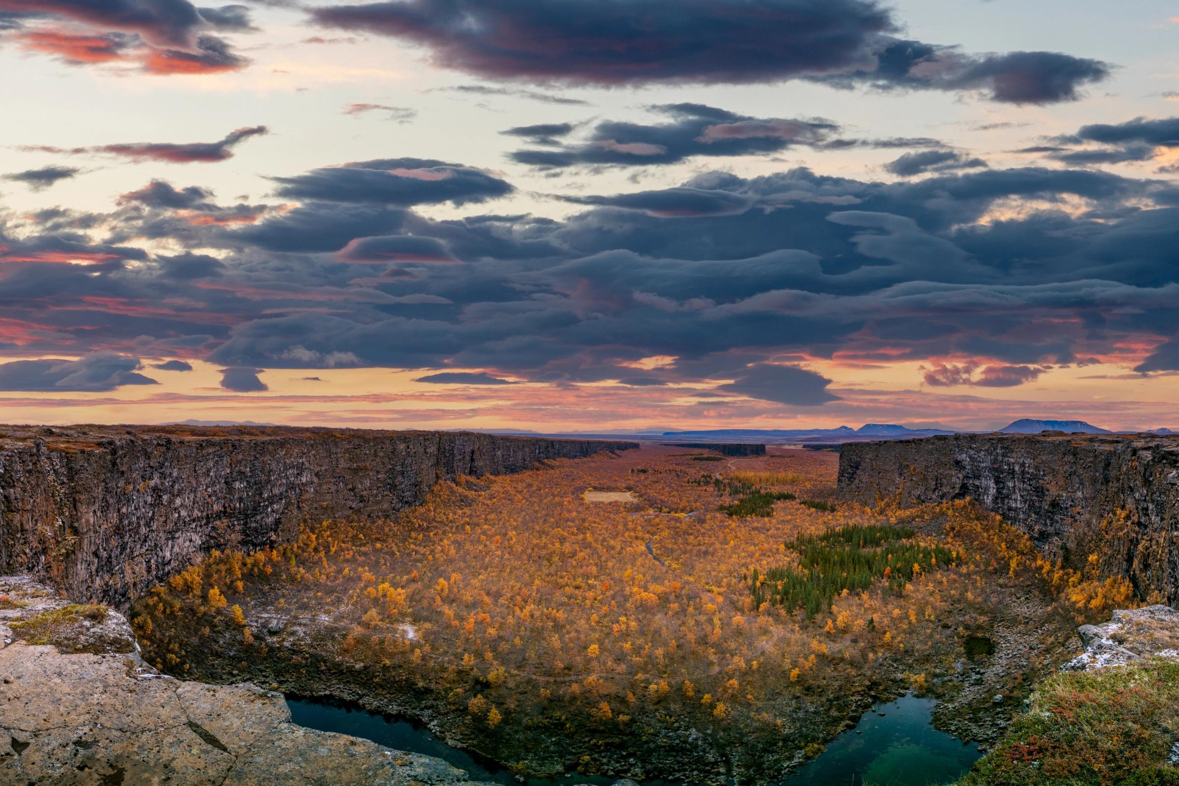 un cañón con un río en medio y una puesta de sol de fondo.