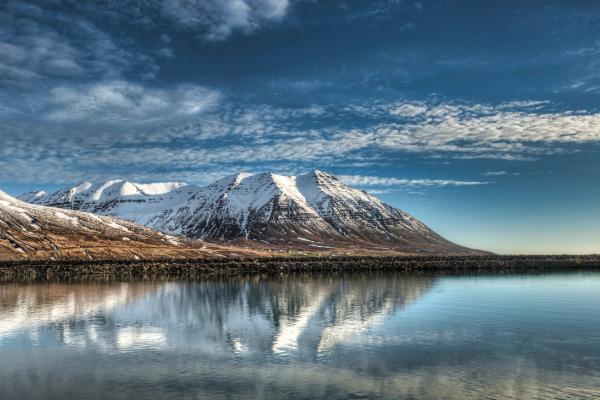 a lake surrounded by snow covered mountains on a cloudy day at Olafsfjordur in Iceland.