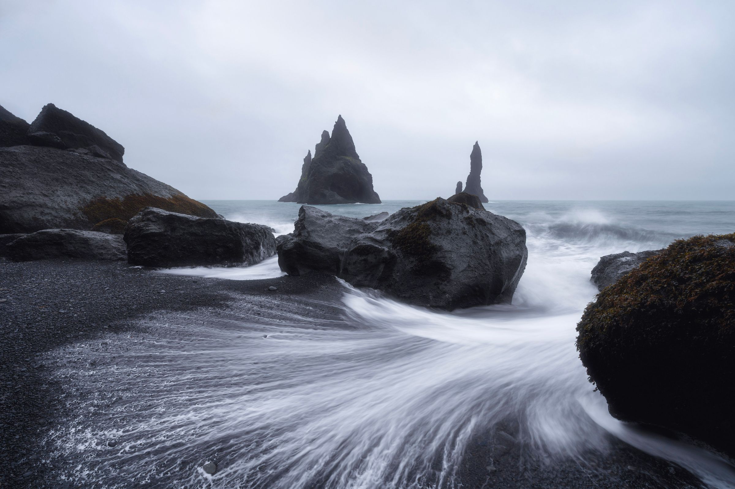 une photo en pose longue des vagues se brisant sur une plage rocheuse à Reynisfjara en Islande.