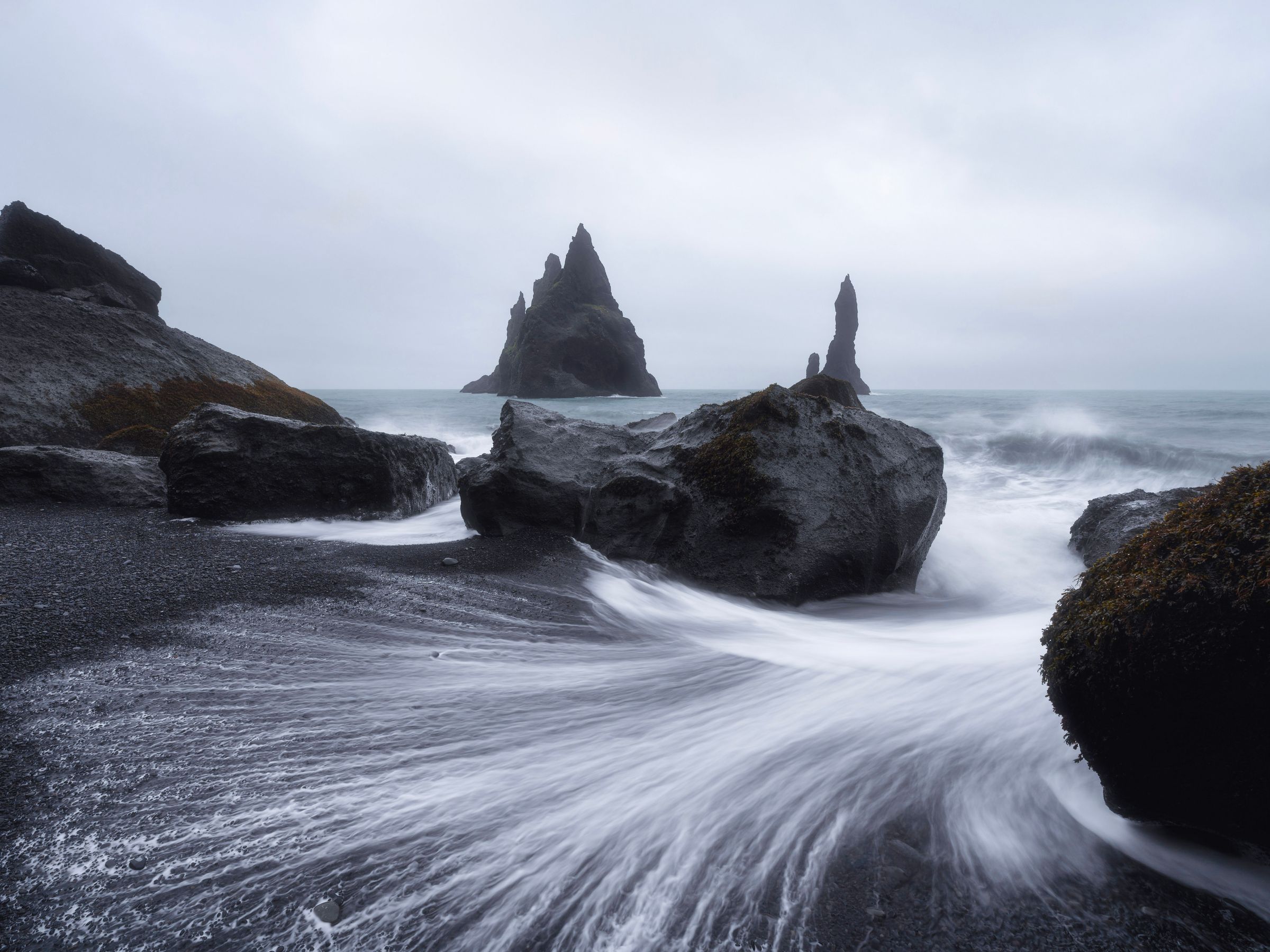 une photo en pose longue des vagues se brisant sur une plage rocheuse à Reynisfjara en Islande.