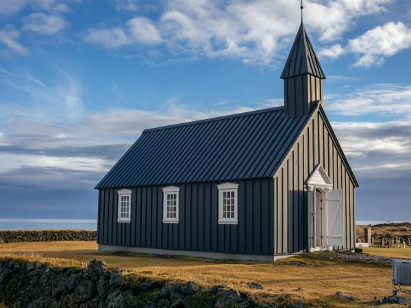una pequeña iglesia negra con un campanario en medio de un campo.