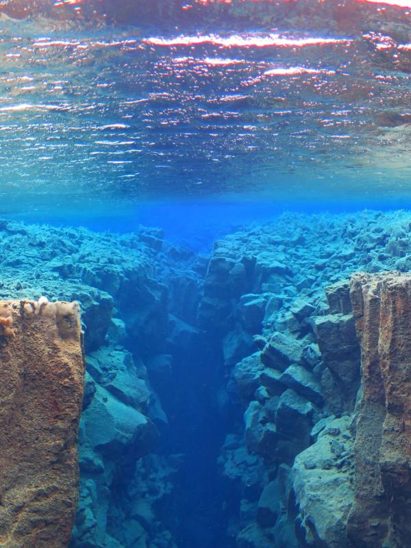 Underwater view of a deep, rocky crevice in clear blue water, with the surface visible above.