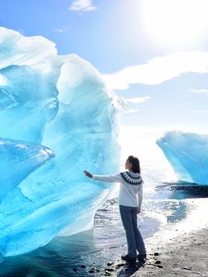 a woman is standing on a beach touching a large iceberg, Iceland
