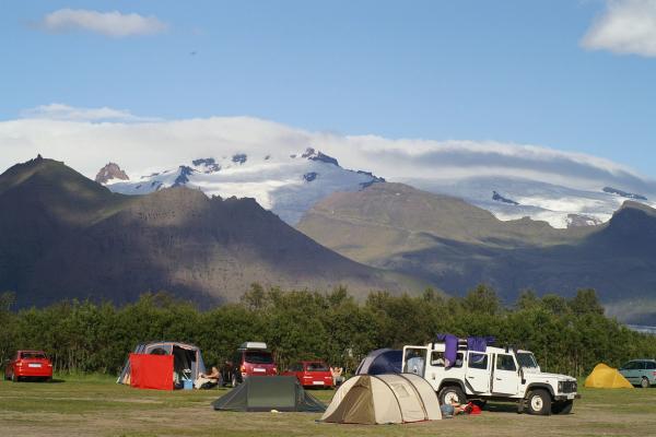 un groupe de tentes et de voitures est garé dans un champ avec des montagnes en arrière-plan .