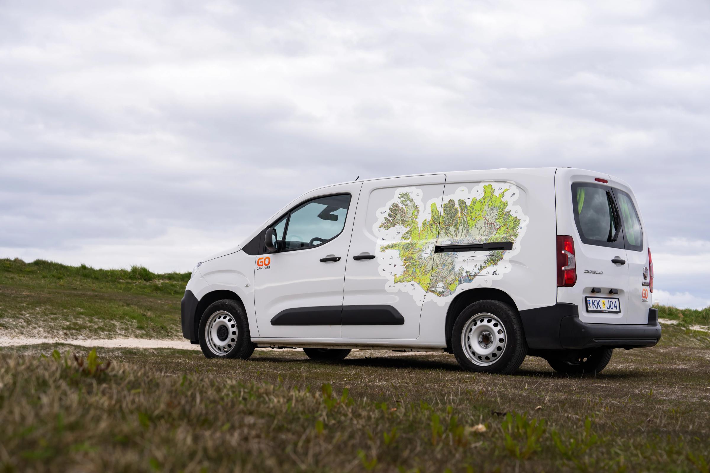 Vista trasera en tres cuartos de una autocaravana compacta para 2 personas, con las puertas cerradas, sobre una pradera en Islandia