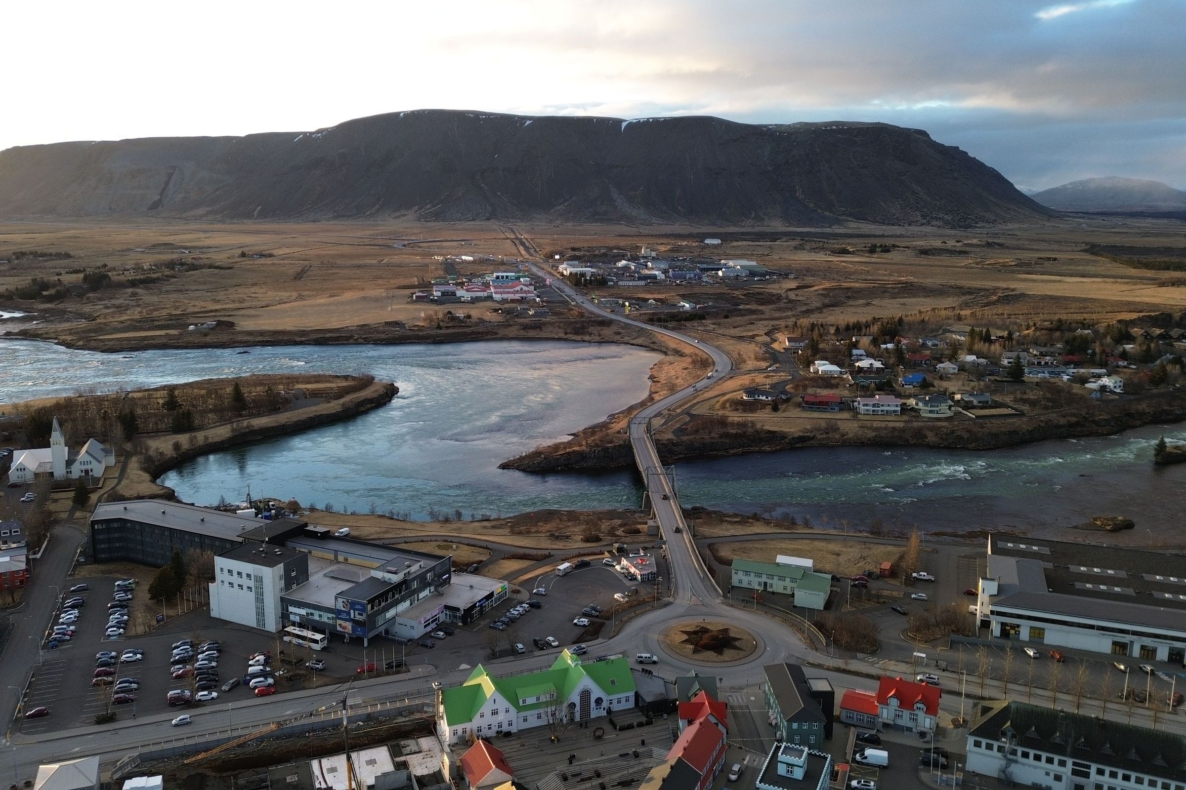 Vista aérea de un pueblo junto a un río y una montaña de fondo