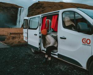 a woman is getting out of a white van in front of a waterfall .