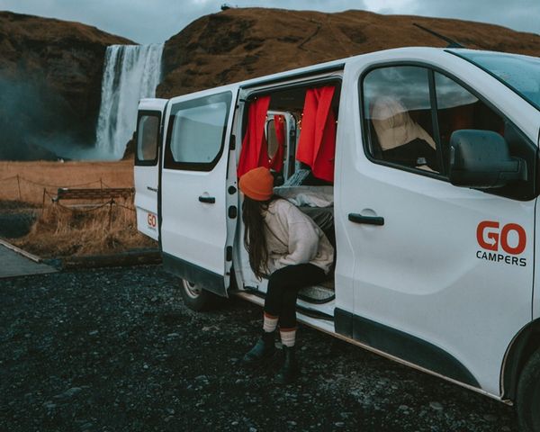 a woman is getting out of a white van in front of a waterfall .