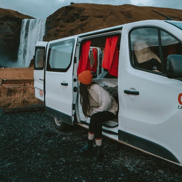 a woman is getting out of a white van in front of a waterfall .
