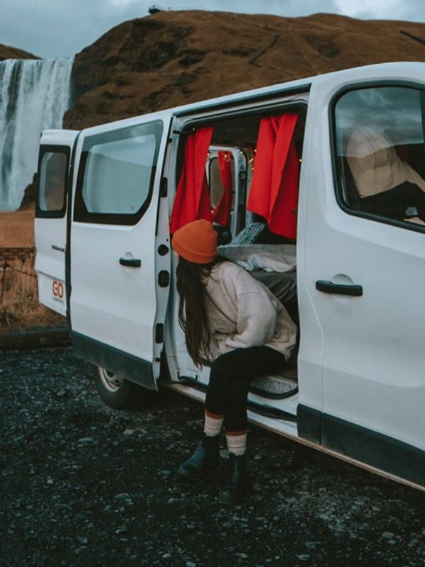 a woman is getting out of a white van in front of a waterfall .