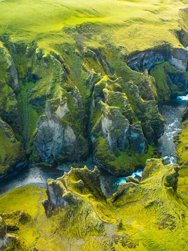 Aerial view of a winding river flowing through a deep, mossy green canyon.