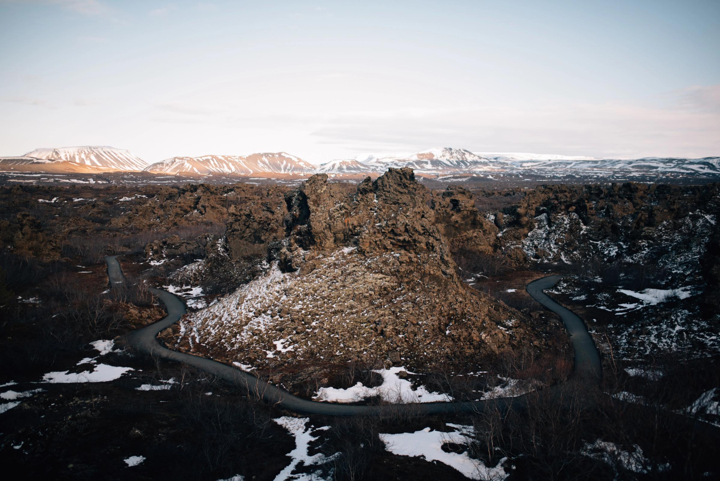 Carretera sinuosa que atraviesa un paisaje volcánico escarpado y nevado, con montañas lejanas cubiertas de nieve.