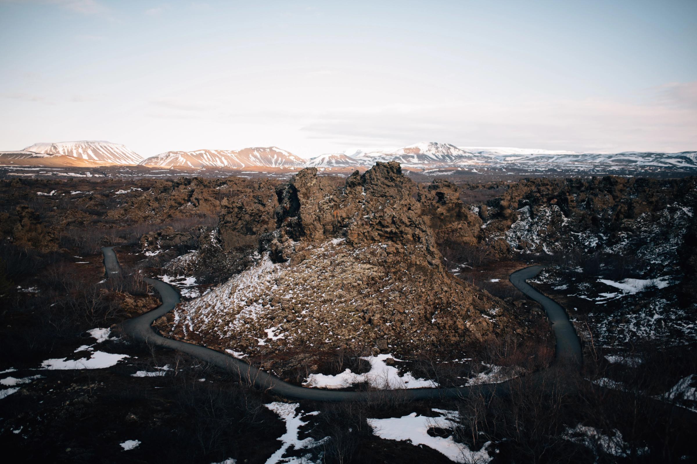 Carretera sinuosa que atraviesa un paisaje volcánico escarpado y nevado, con montañas lejanas cubiertas de nieve.