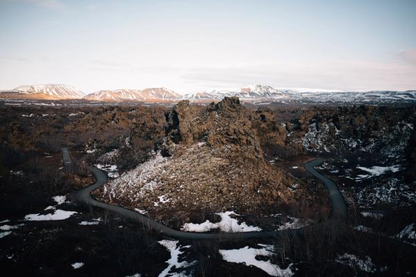 Winding road through a rugged, snowy volcanic landscape with distant snow-capped mountains.