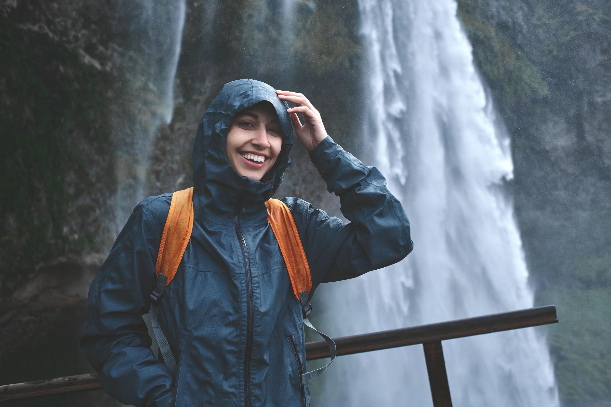 Chica con un chubasquero delante de una cascada en Islandia
