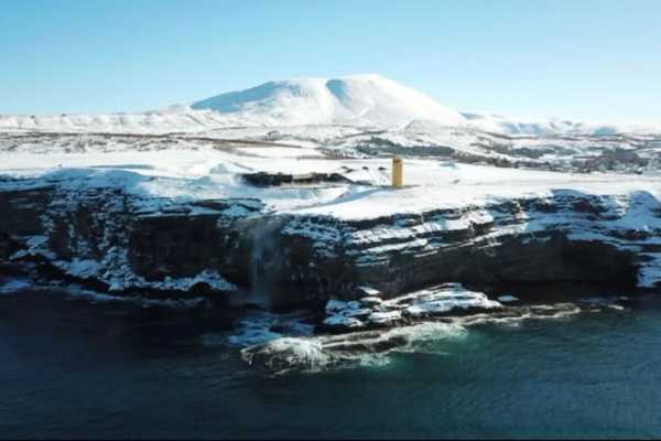 Snowy cliffs with a waterfall flowing into the ocean, a yellow lighthouse, and distant snow-capped mountains.