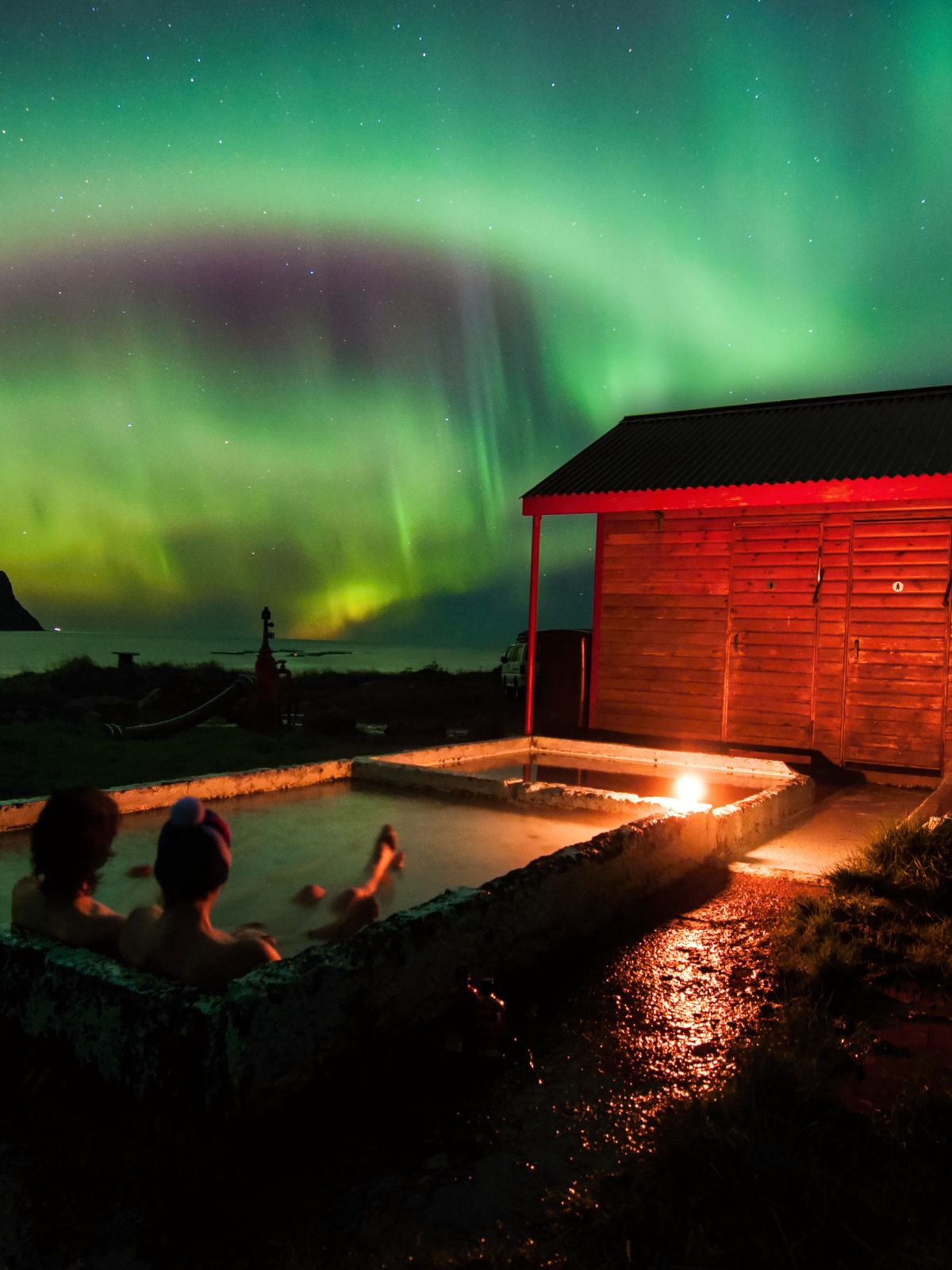 two people are sitting in a hot tub under the aurora borealis .