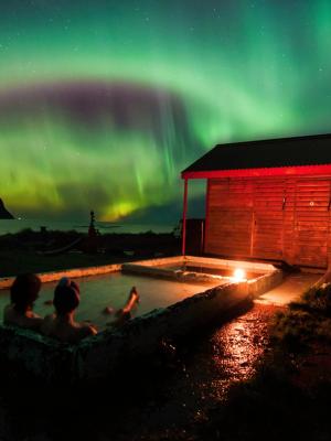 two people are sitting in a hot tub under the aurora borealis .