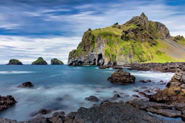 a long exposure photo of a rocky shoreline with a mountain in the background .