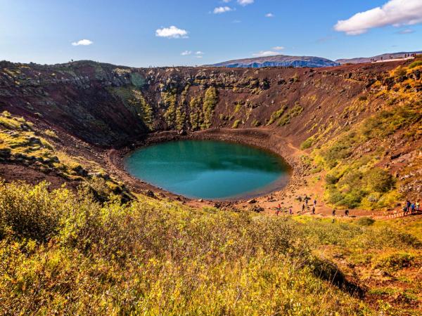 a group of people are standing around a large lake in the middle of a crater .