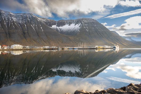 Snow-capped mountains and a village reflecting in a calm fjord.