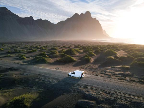 an aerial view of a white van driving down a dirt road in the desert .