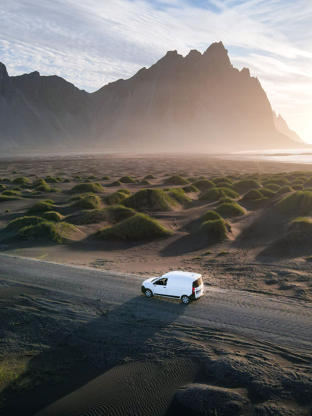 an aerial view of a white van driving down a dirt road in the desert .