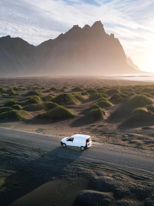 an aerial view of a white van driving down a dirt road in the desert .