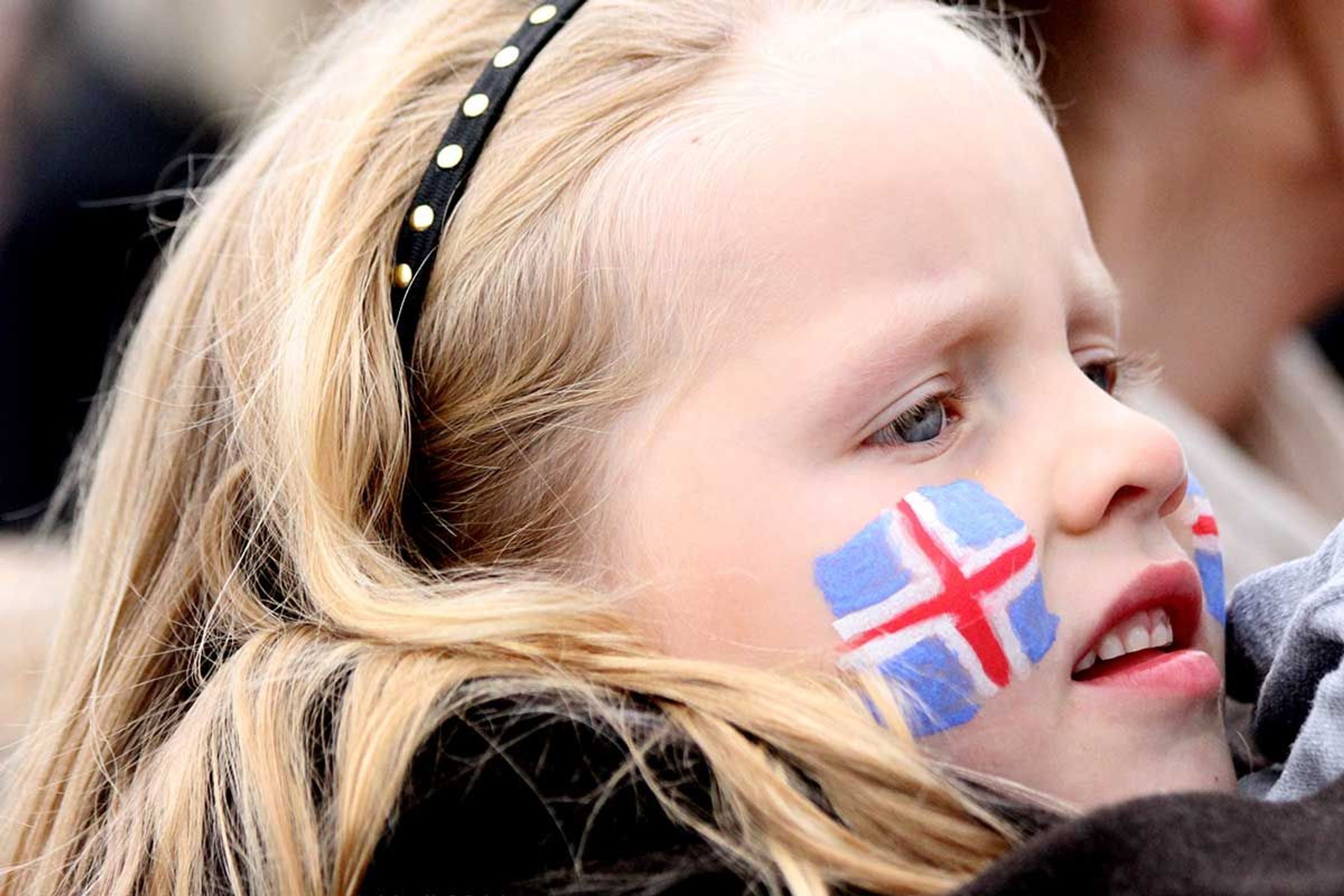 Una chica joven y rubia con la bandera de Islandia pintada en la mejilla.