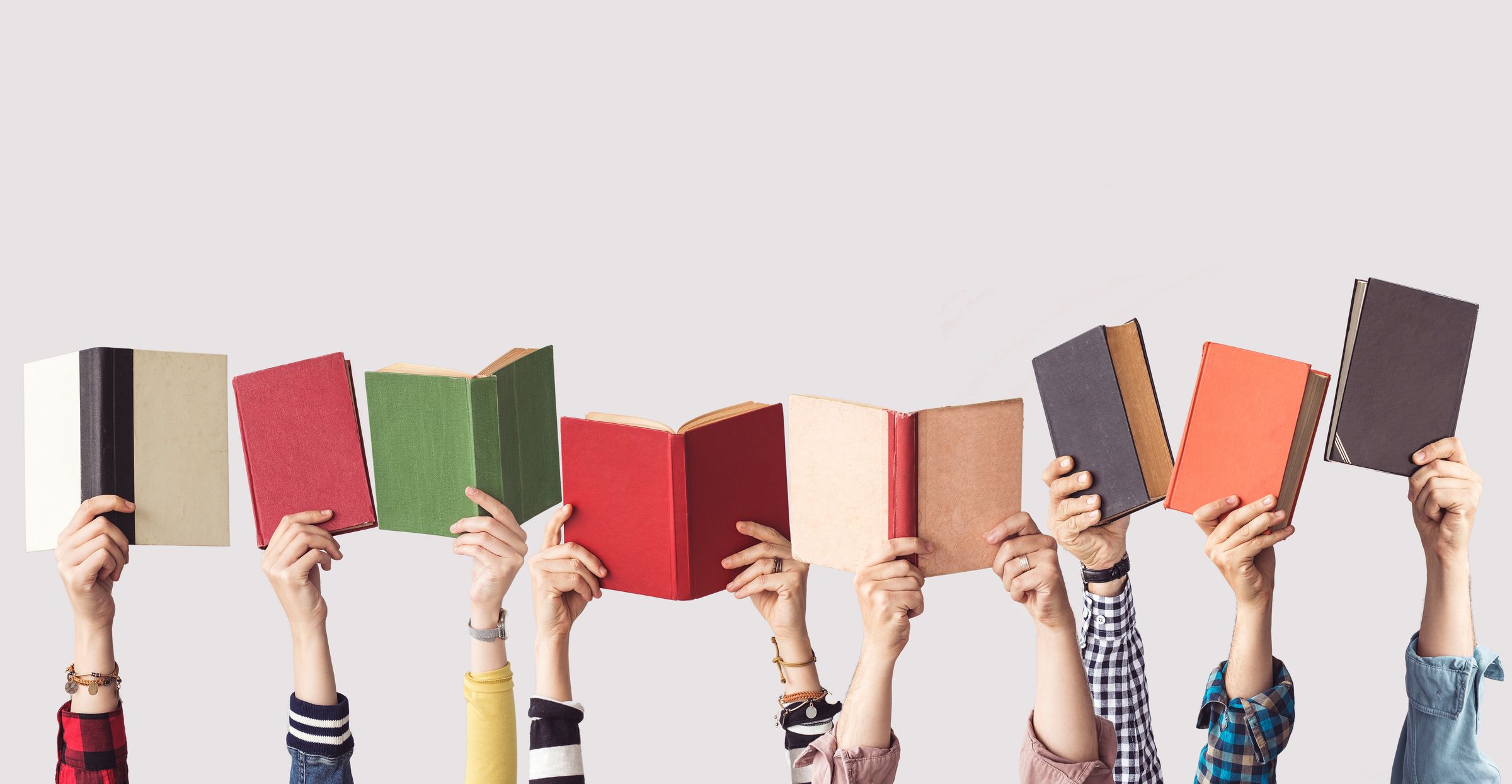 Many hands holding up colorful books.