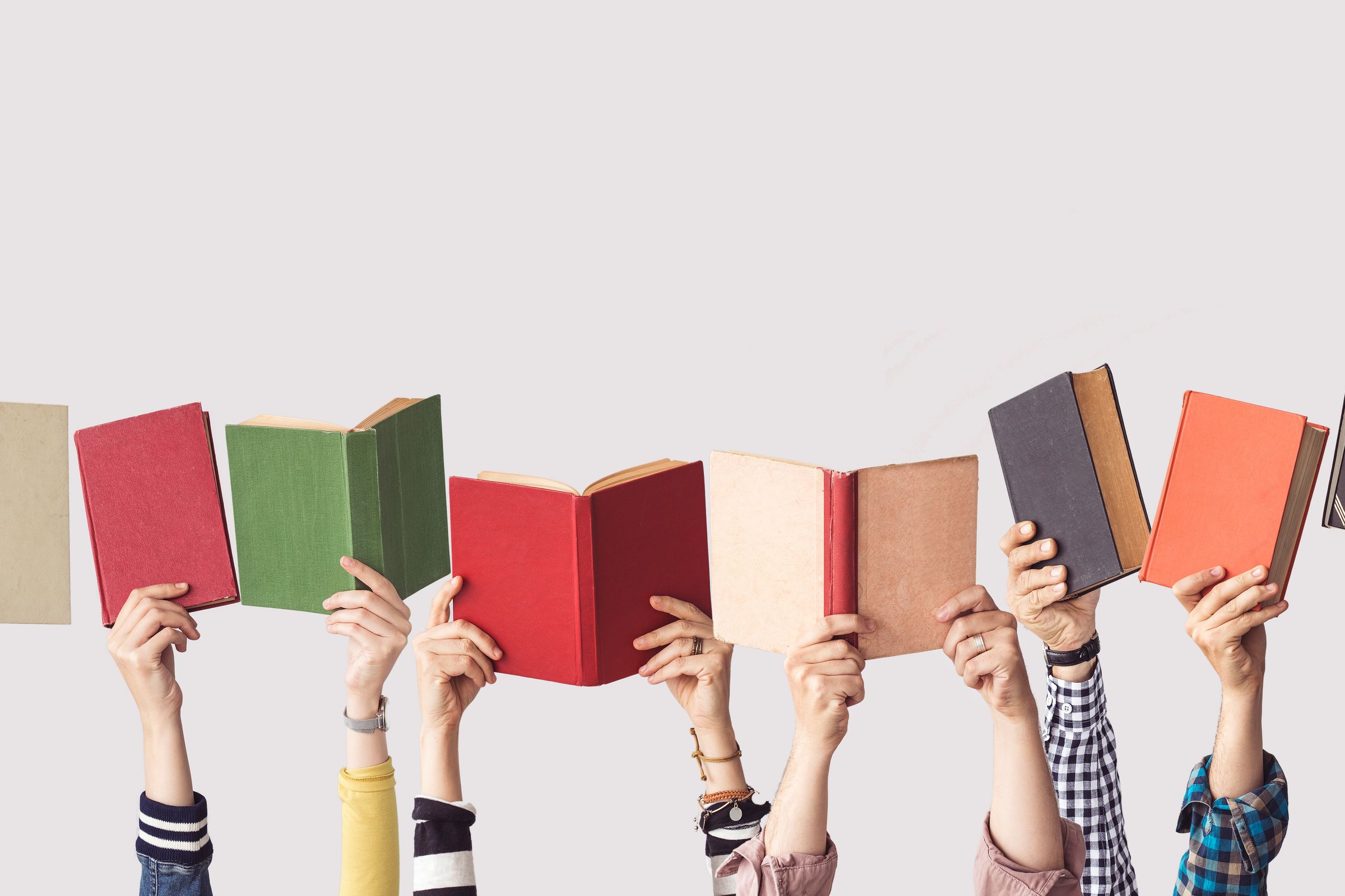 Many hands holding up colorful books.