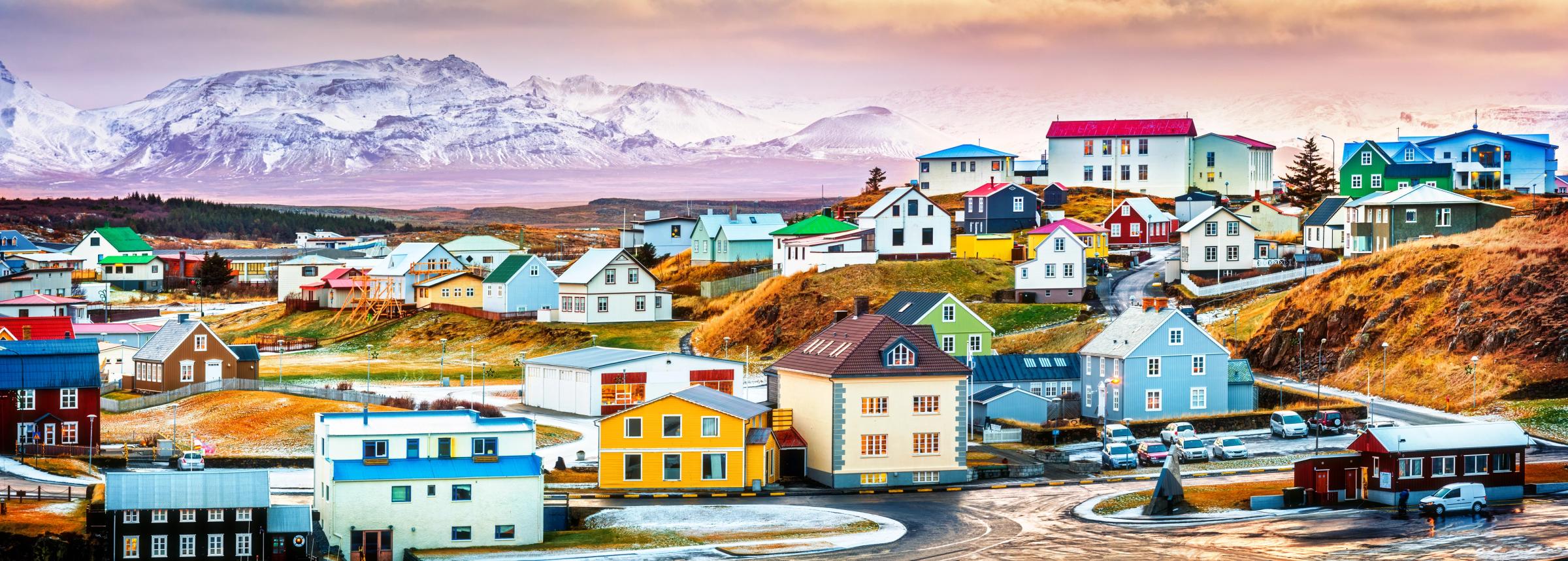 Colorful town on rolling hills with snow-capped mountains in the background.