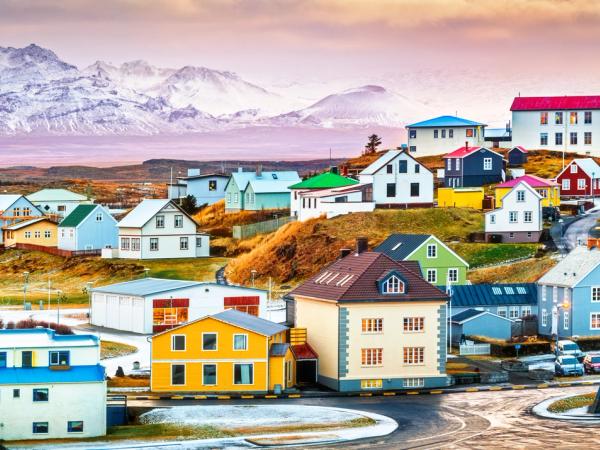 Colorful town on rolling hills with snow-capped mountains in the background.