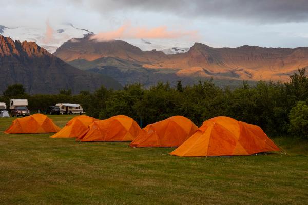 orange tents on a meadow with mountains on the background