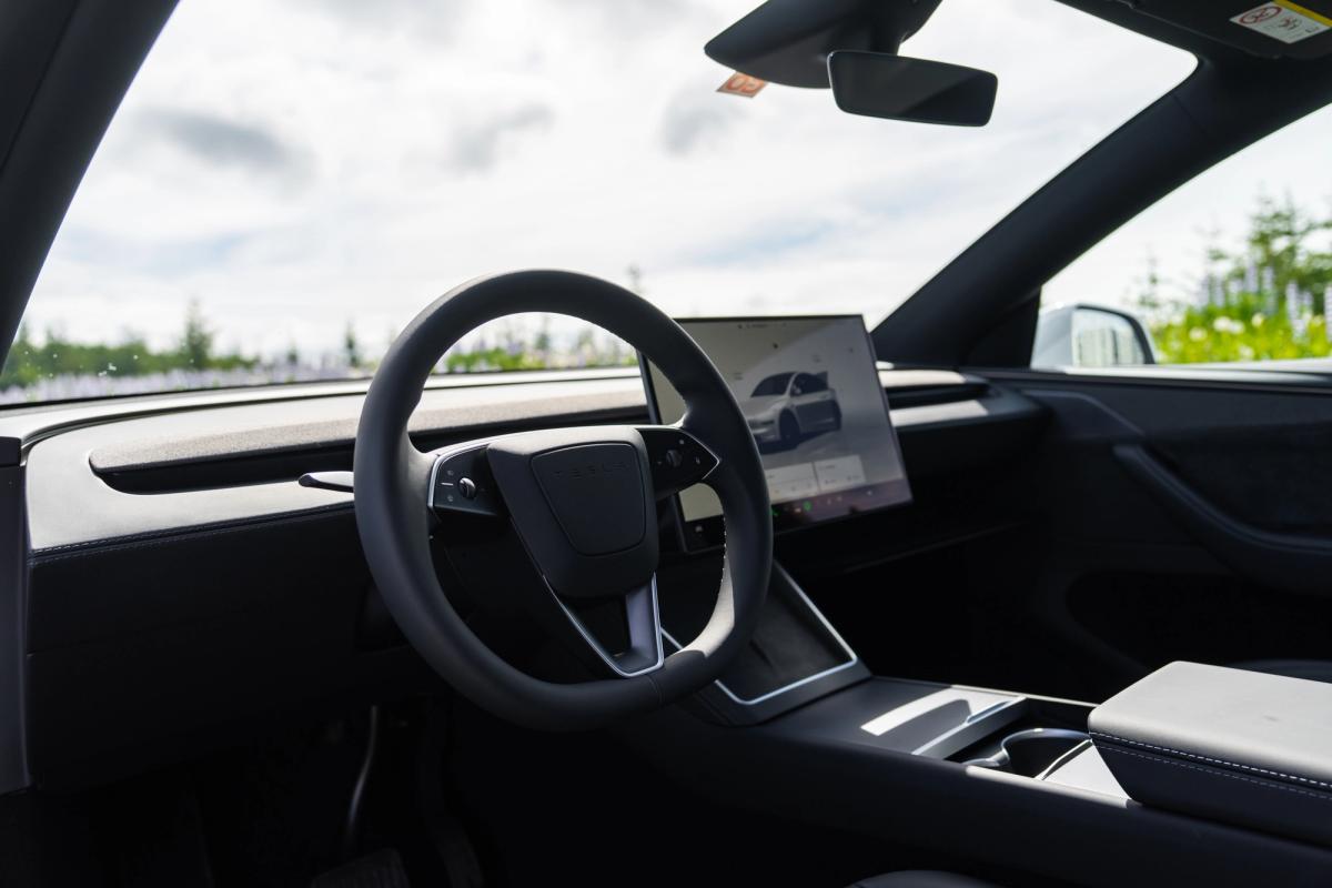 Vista del conductor de día Salpicadero y volante de un Tesla Model Y con un paisaje verde y luminoso en el exterior, vehículo para recorrer Islandia por cuenta propia
