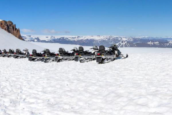 a group of people are riding snowmobiles down a snow covered slope .