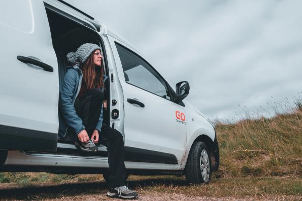 Girl sitting at the door of a white campervan