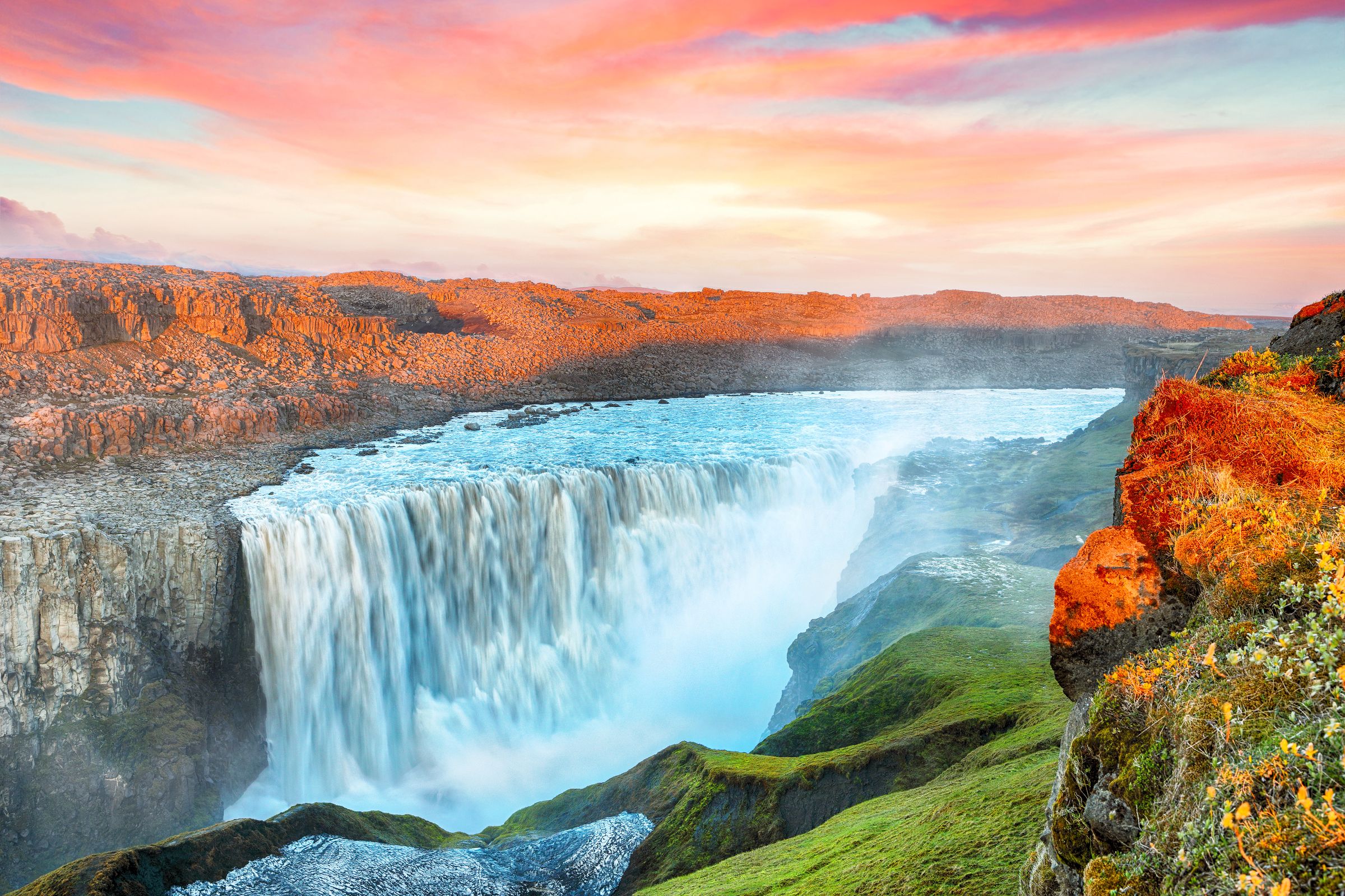 a waterfall in the middle of a valley with a sunset in the background at Dettifoss in North Iceland..
